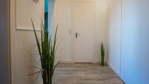 Un pasillo con una puerta blanca, un cuadro en la pared y dos plantas en macetas.