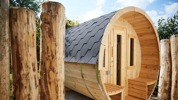 A wooden cylindrical structure with a curved roof and a door, surrounded by wooden posts. - Haus Daglind Apartment 3 mit Saunafass und Balkon (Büsum)