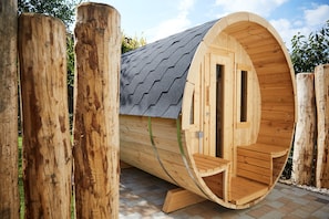 A wooden cylindrical structure with a curved roof and a door, surrounded by wooden posts. - Haus Daglind Apartment 3 mit Saunafass und Balkon (Büsum)
