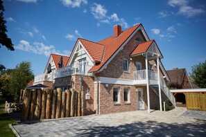 A two-story house with a red-tiled roof, white trim, and a wooden fence.