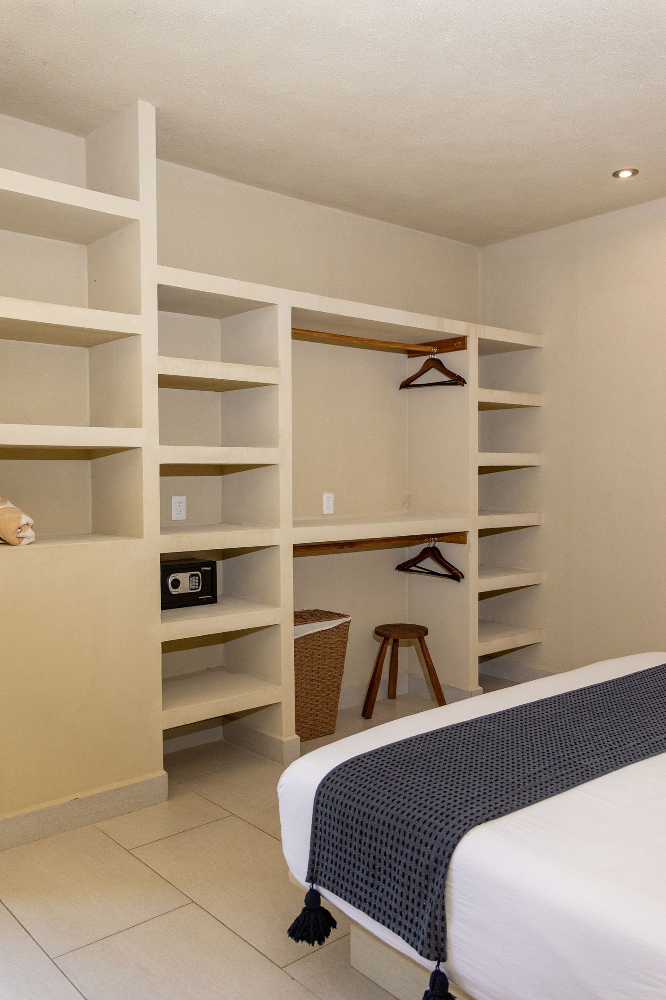 Un dormitorio con una cama, un armario grande con varios estantes, una radio y una cesta de mimbre.