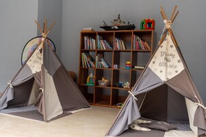Una habitación con dos tiendas de campaña pequeñas, una estantería llena de libros y un barco de juguete en un estante.
