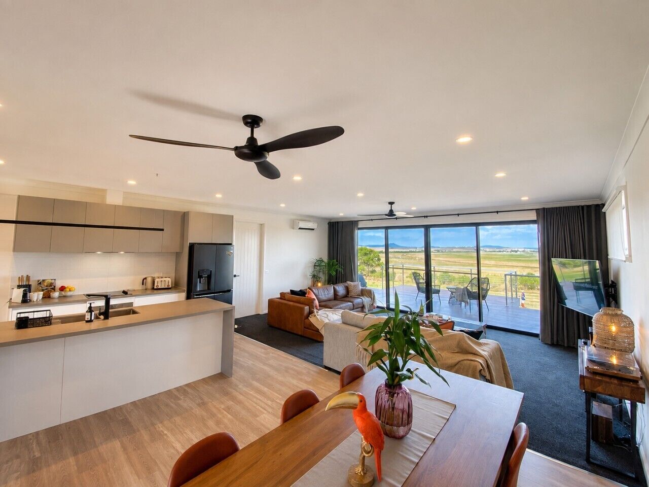 A modern interior with a kitchen, dining area, and living space with a large window overlooking a landscape.
