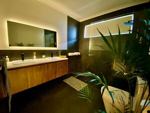 A modern bathroom with a wooden vanity, a large mirror, and a potted plant.
