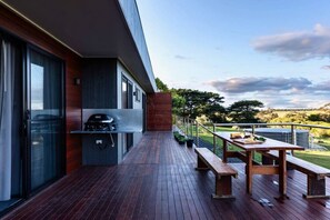 A modern outdoor deck with a grill, wooden benches, and a view of the countryside.