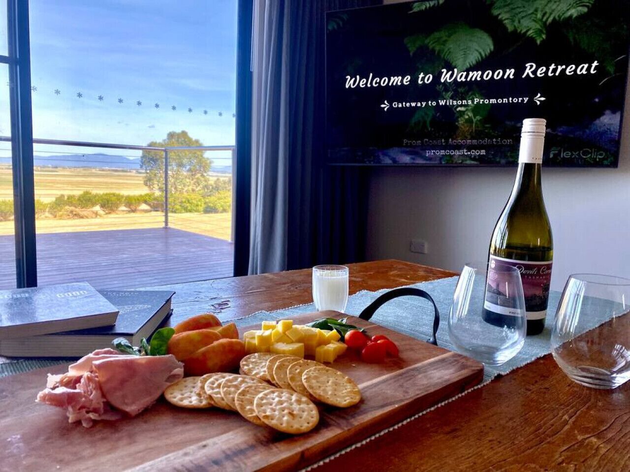 A welcome sign for Wamoon Retreat, a glass of wine, and a board with cheese, crackers, and ham.