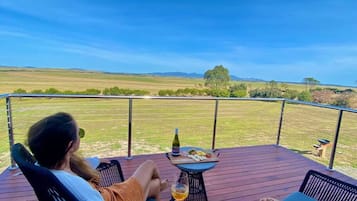 A person relaxing on a deck with a table and chairs, overlooking a grassy field.