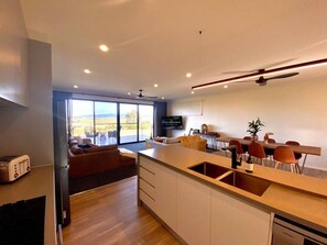 A modern kitchen with a large island, a dining area with red chairs, and a view of the outdoors through large windows.