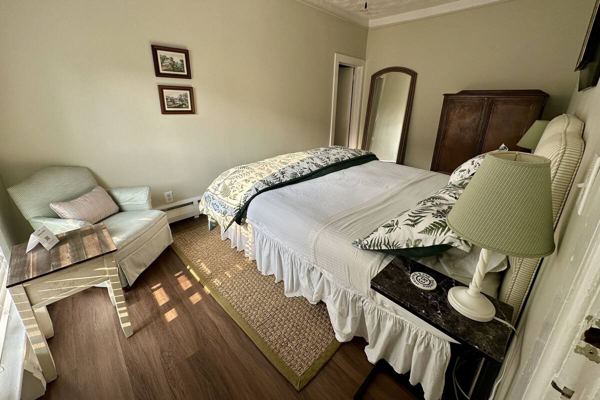 A bedroom with a bed, a chair, a desk, a mirror, and a ceiling fan.