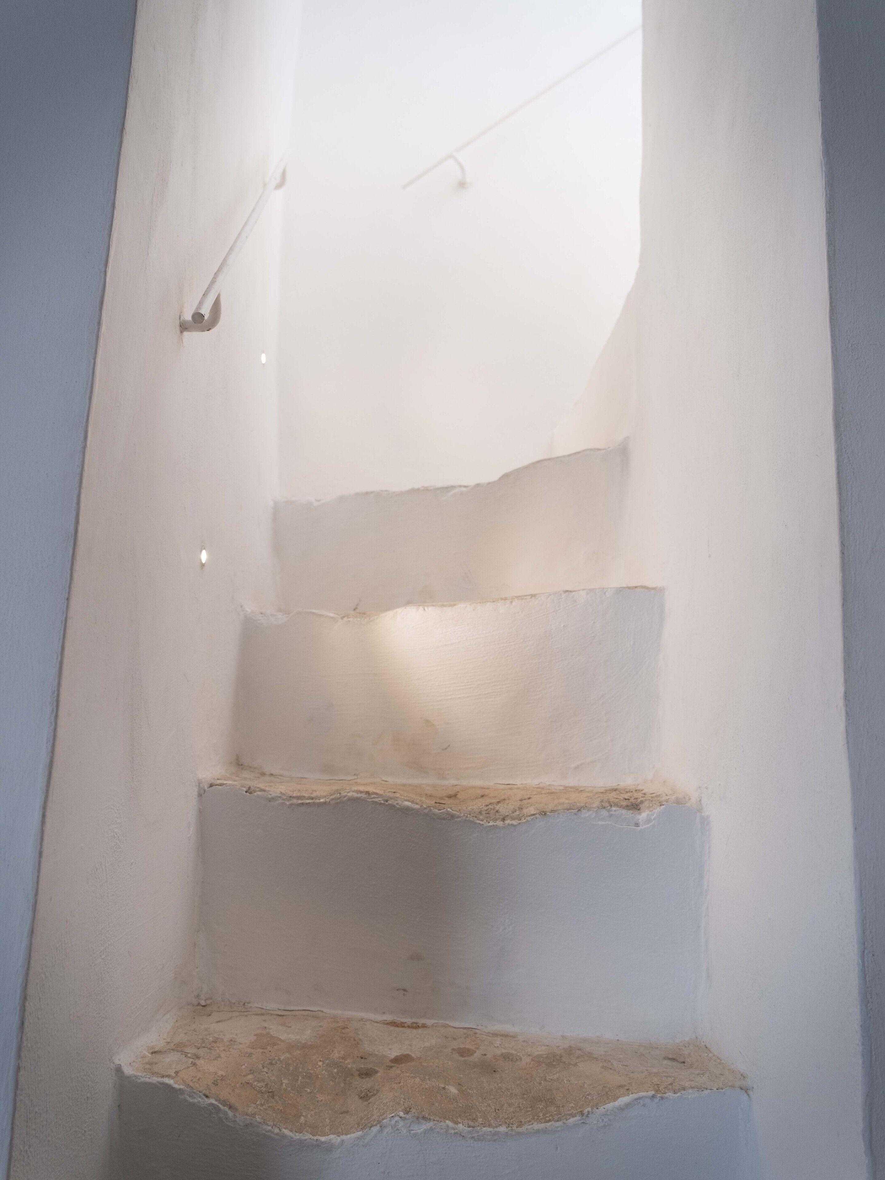A staircase with white walls and a light fixture at the top.