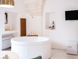 A modern bathroom with a freestanding bathtub, a wooden door, a mounted TV, and a wine bottle on a shelf.