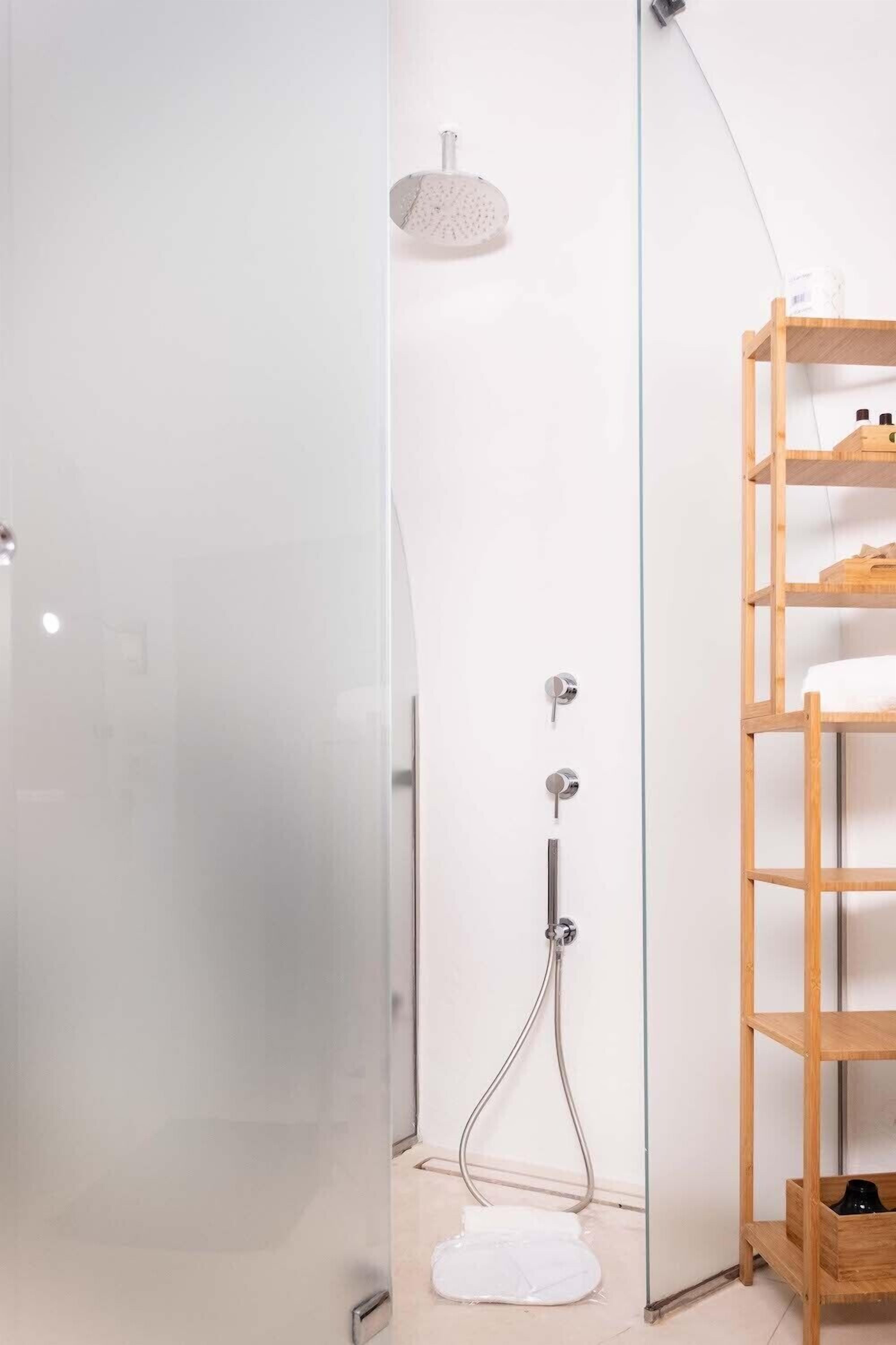 Ein modernes Badezimmer mit Duschkabine aus Glas, einer Holzregalanlage und einem weißen Handtuch auf dem Boden.