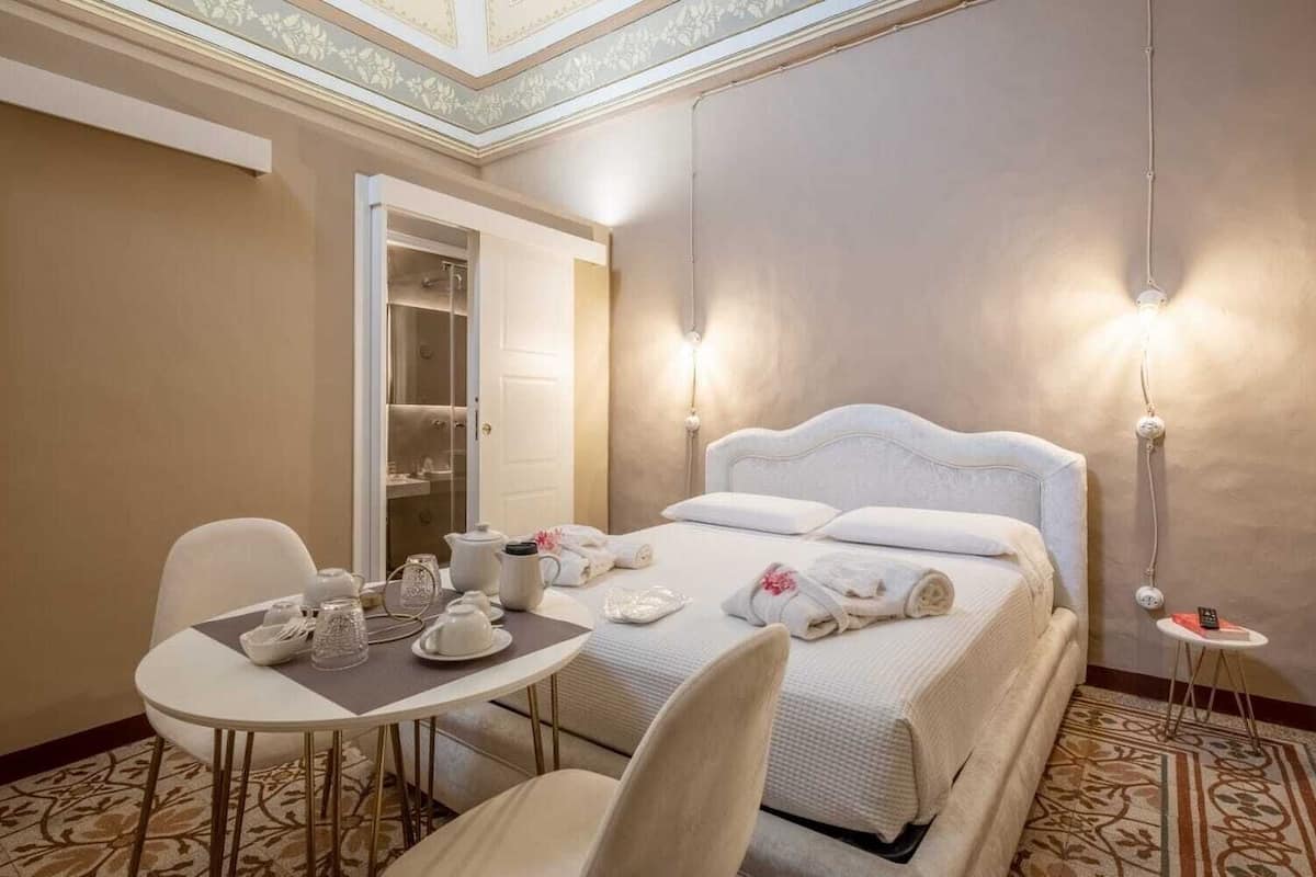 Una habitació d'hotel amb un llit ben arropat, una taula de dinar amb joc de te i un armari amb mirall.