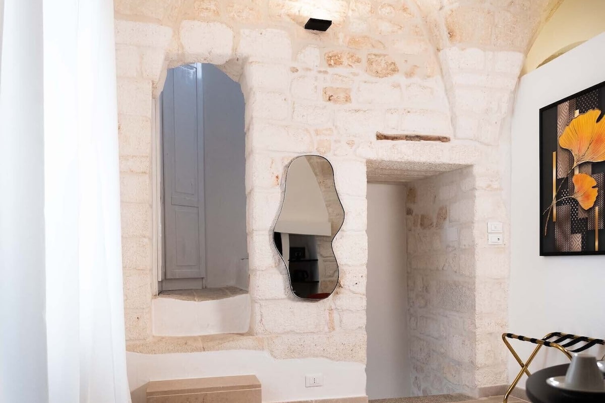 Una habitació amb parets de pedra vista, una porta blanca, un mirall i una obra d'art emmarcada a la paret.