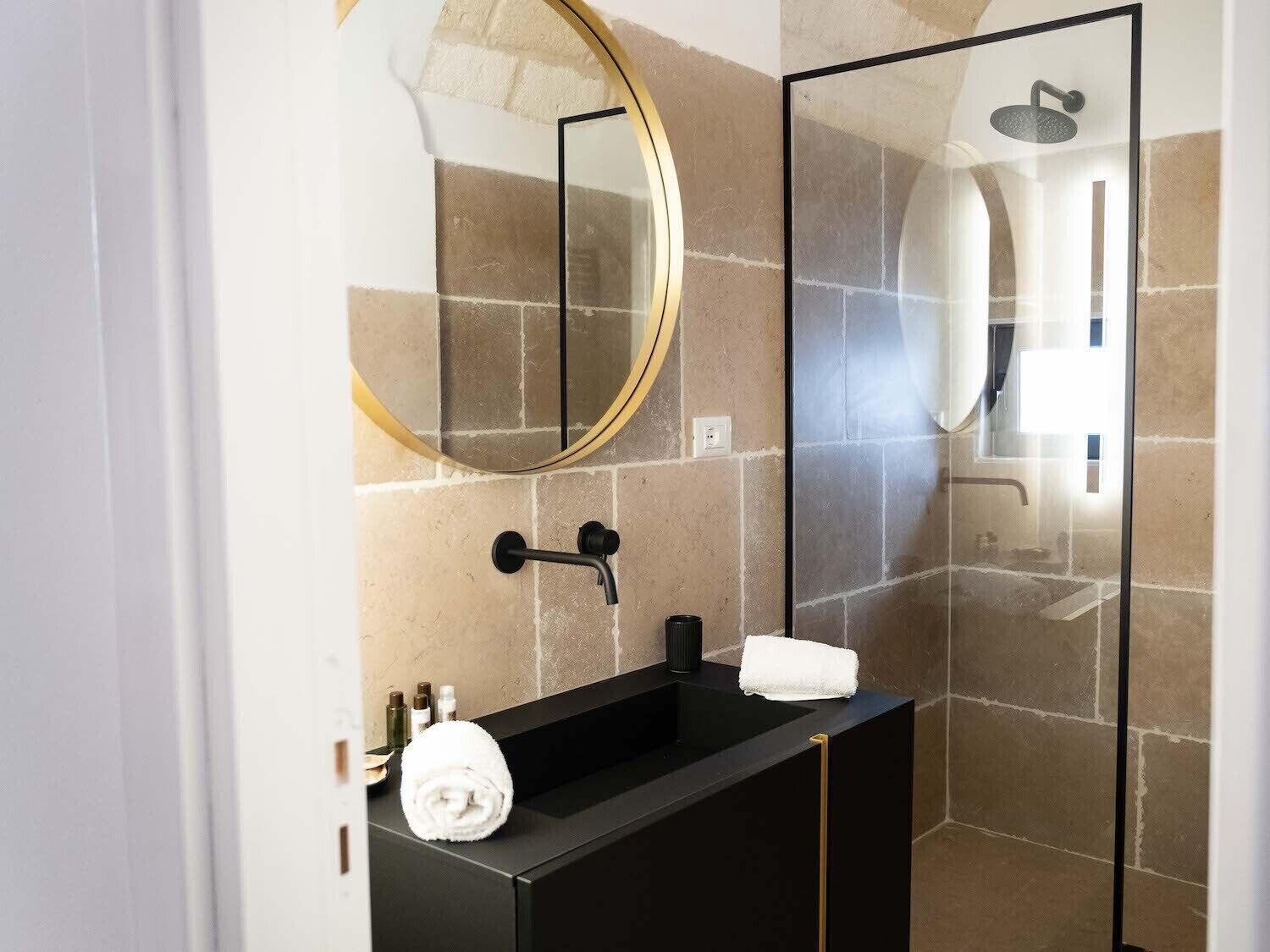 Een moderne badkamer met een zwart wastafel, een ronde spiegel en een douchecabine van glas.