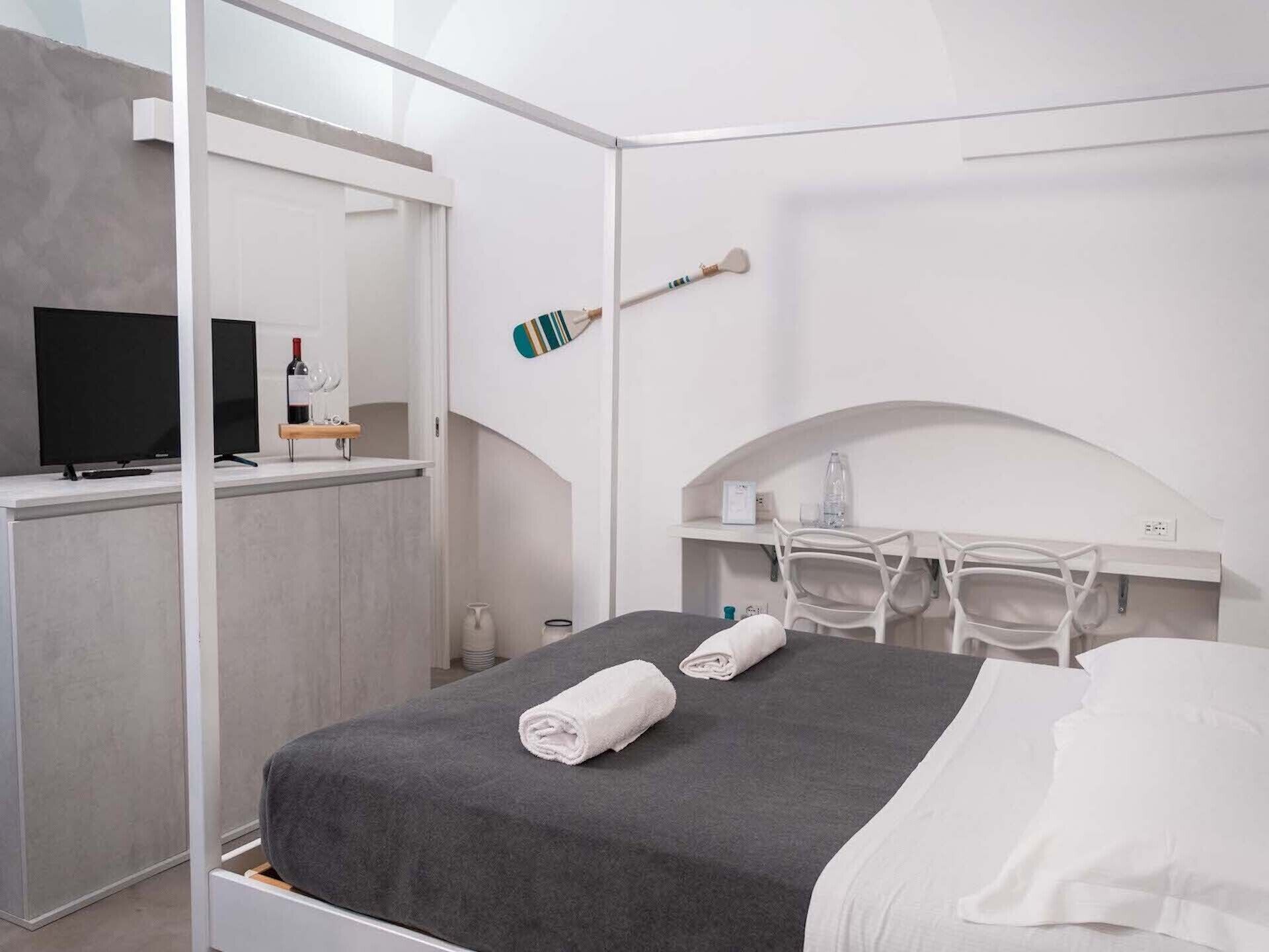 A modern hotel room with a bed, a TV, a minibar, and a desk with chairs.