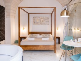 A four-poster bed with a wooden frame, a large abstract painting above it, and a round table with chairs in the foreground.
