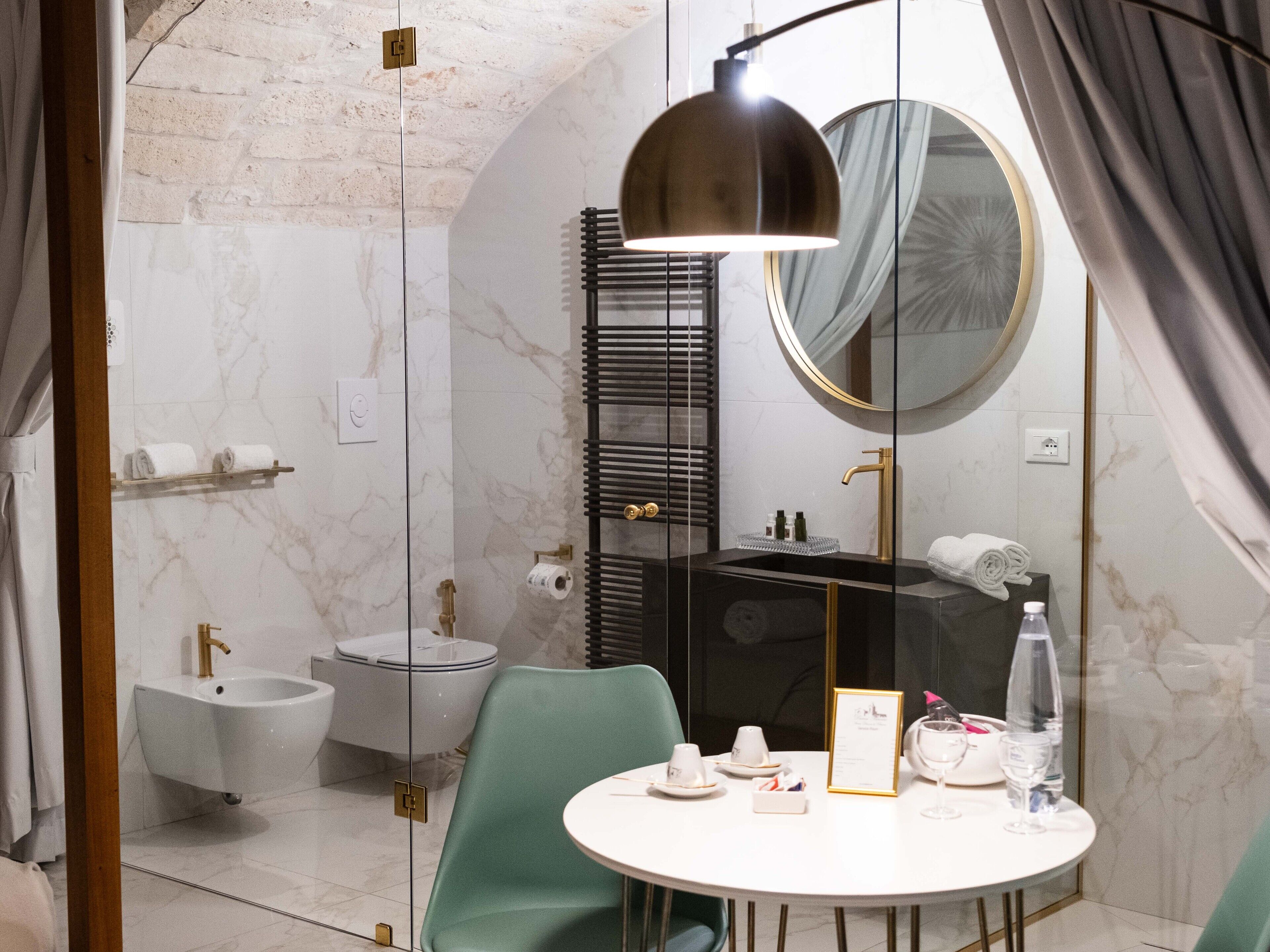 Ein modernes Badezimmer mit einer in Glas eingefassten Dusche, einem weißen Waschbecken, einem goldenen Wasserhahn und einem runden Spiegel.