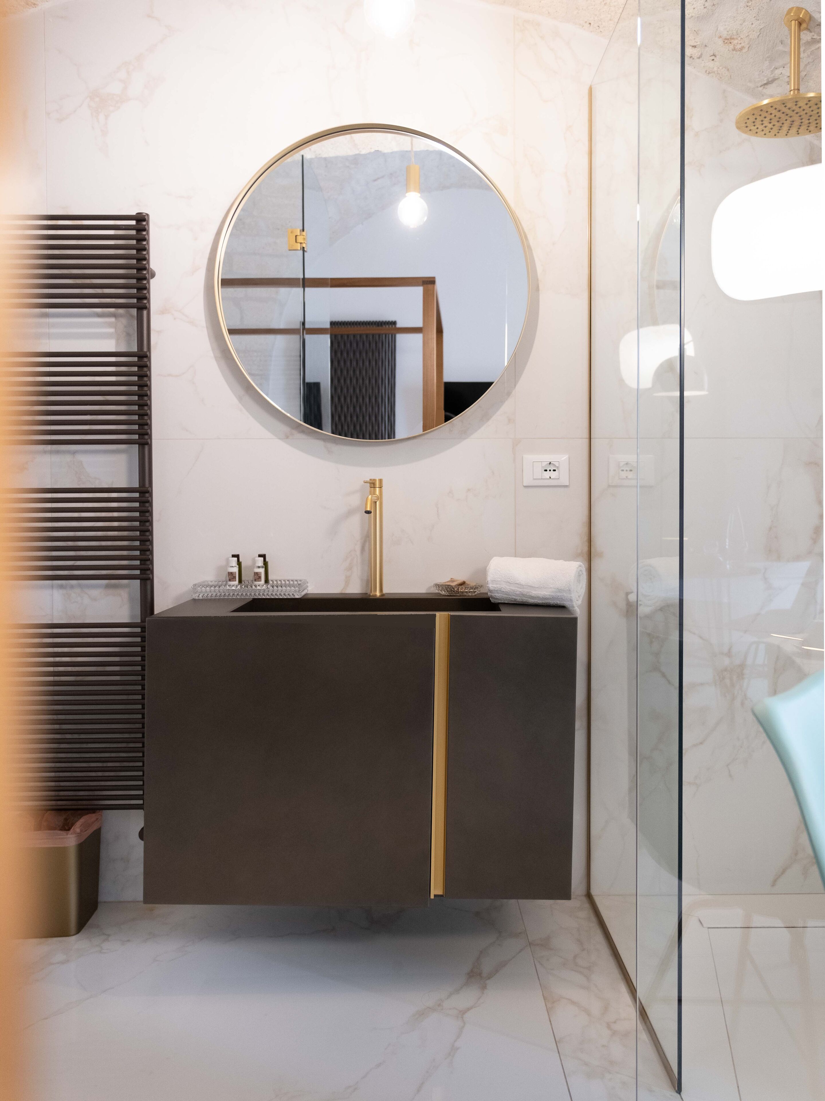 Un bagno moderno con uno specchio rotondo, un mobile vanitario scuro e un box doccia in vetro.