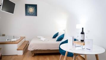 A modern hotel room with a bed, a desk, a round table, a bottle of wine, and a framed picture on the wall.