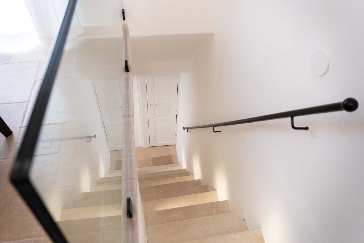 Una scala con corrimano, pareti bianche e una porta in cima.