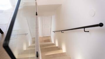 Una scala con corrimano, pareti bianche e una porta in cima.