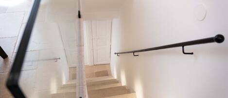 Una escalera con barandilla, paredes blancas y una puerta al final.