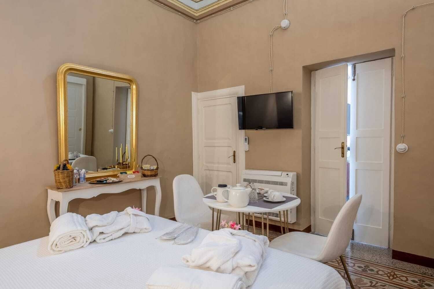 Une chambre d’hôtel comprenant un lit, un bureau avec un miroir, une télévision, une table avec un service à thé et une porte.