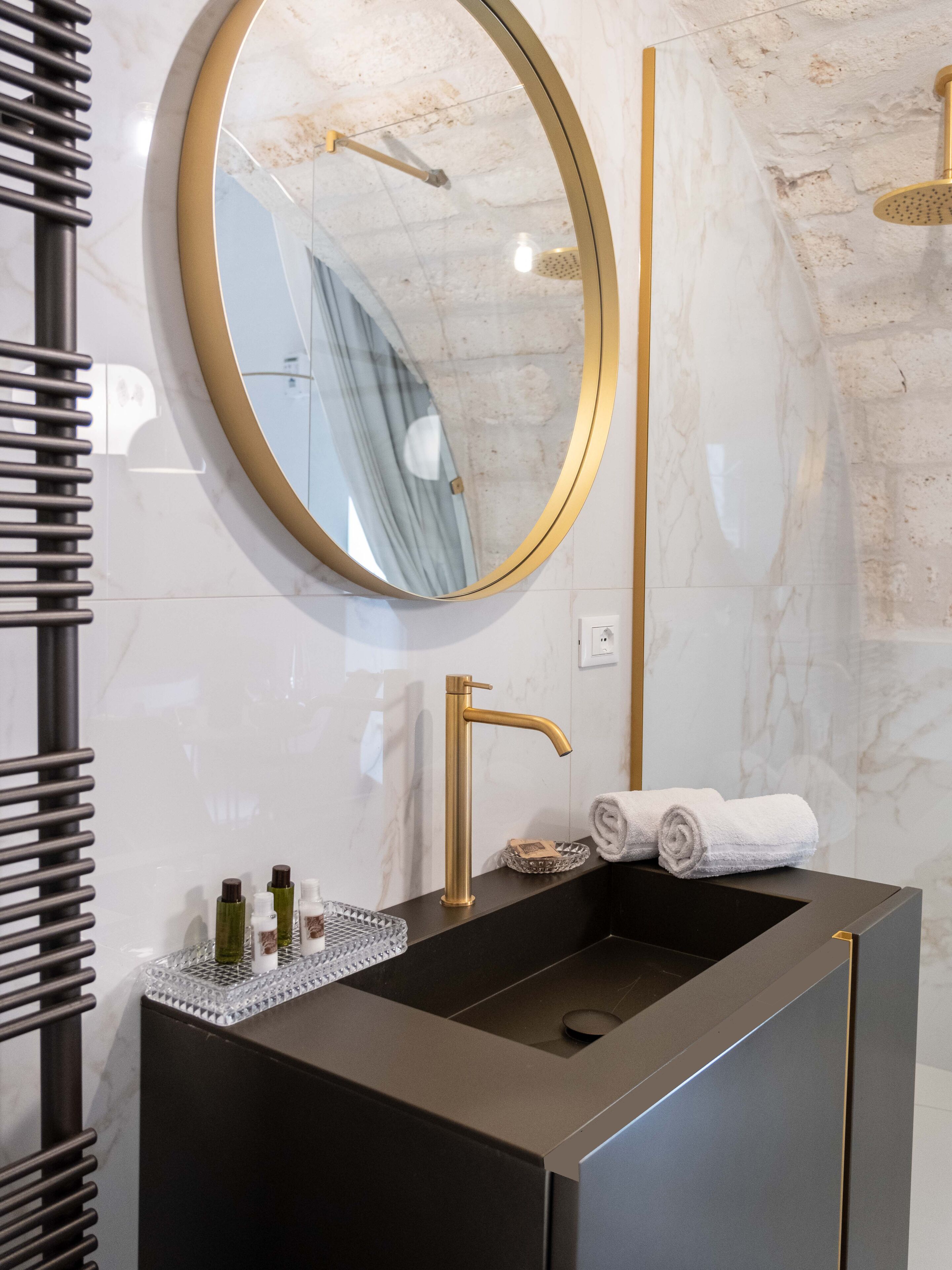 Un baño moderno con tocador negro, accesorios dorados, un espejo redondo y un perchero.