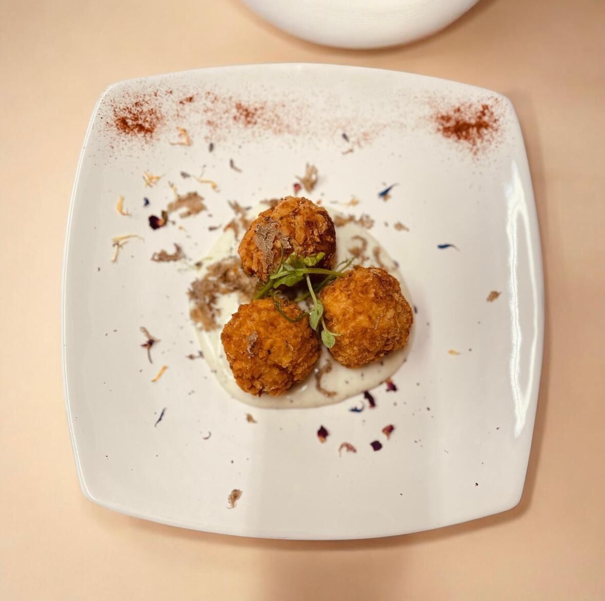 Un plato cuadrado con tres piezas redondas y doradas, probablemente fritas, adornado con hojas verdes, sobre una superficie color beige.