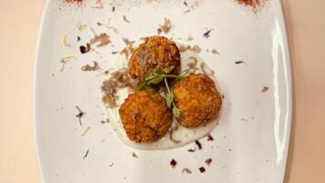 Un plat quadrat amb tres aliments rodons, daurats i fregats, adornat amb fulles verdes, damunt d'una superfície beig.