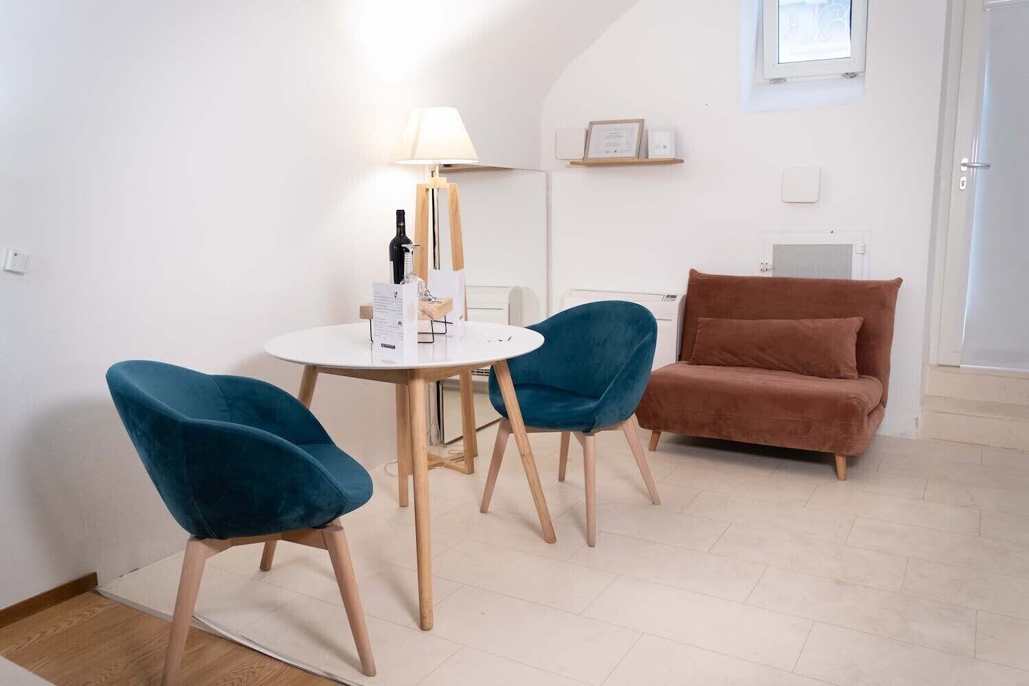 A room with a round table, two blue chairs, a brown sofa, a lamp, and a framed certificate on the wall.