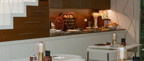 A modern restaurant with white tables and chairs, a staircase with geometric patterns, and a buffet area with food items.