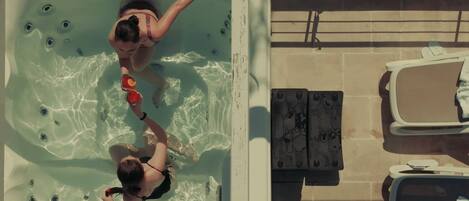 Un jacuzzi con dos personas, una terraza con baldosas y sillones de descanso.