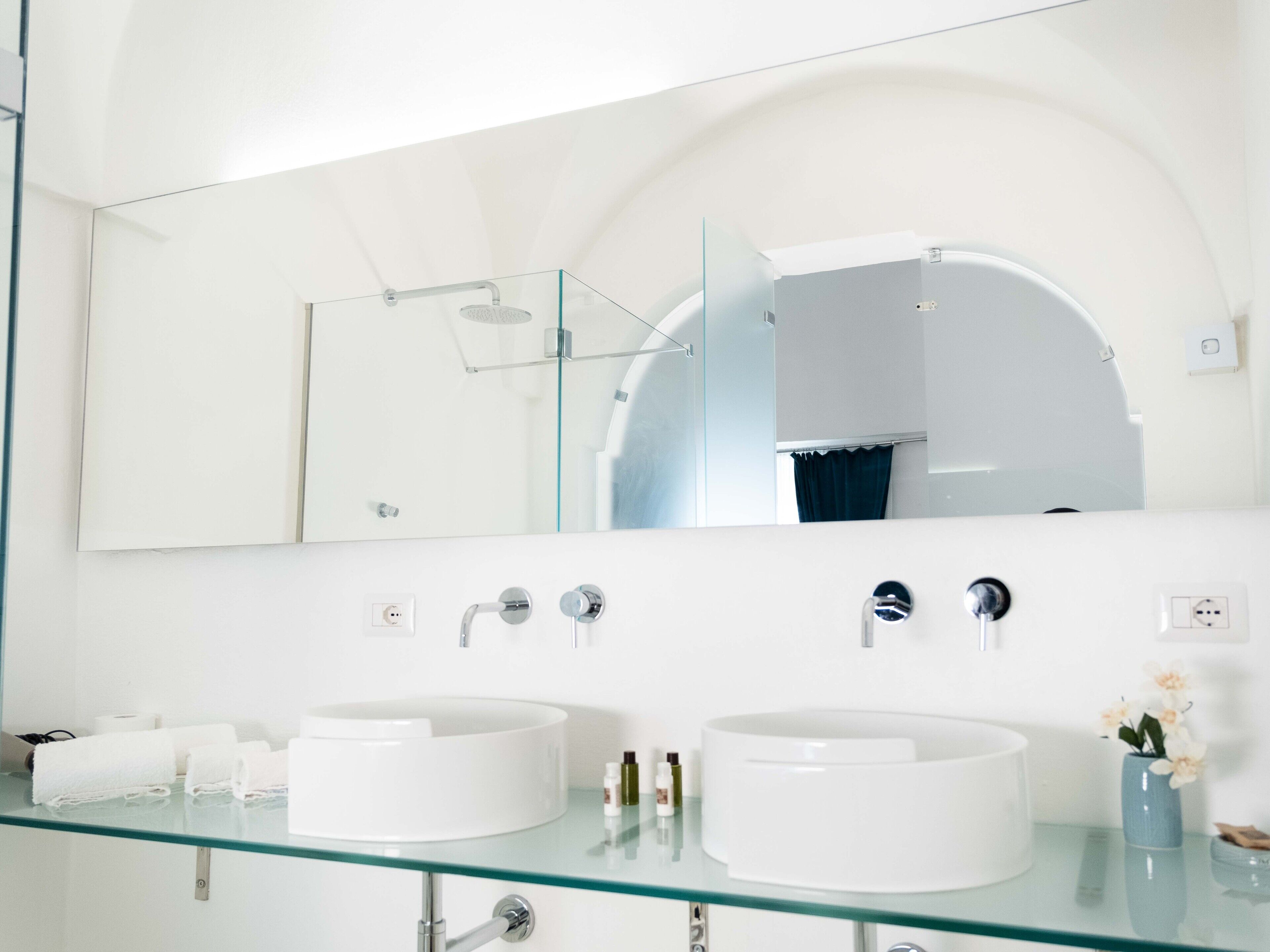 Un baño moderno con dos lavamanos blancos, una encimera de vidrio y un espejo grande en la parte superior.