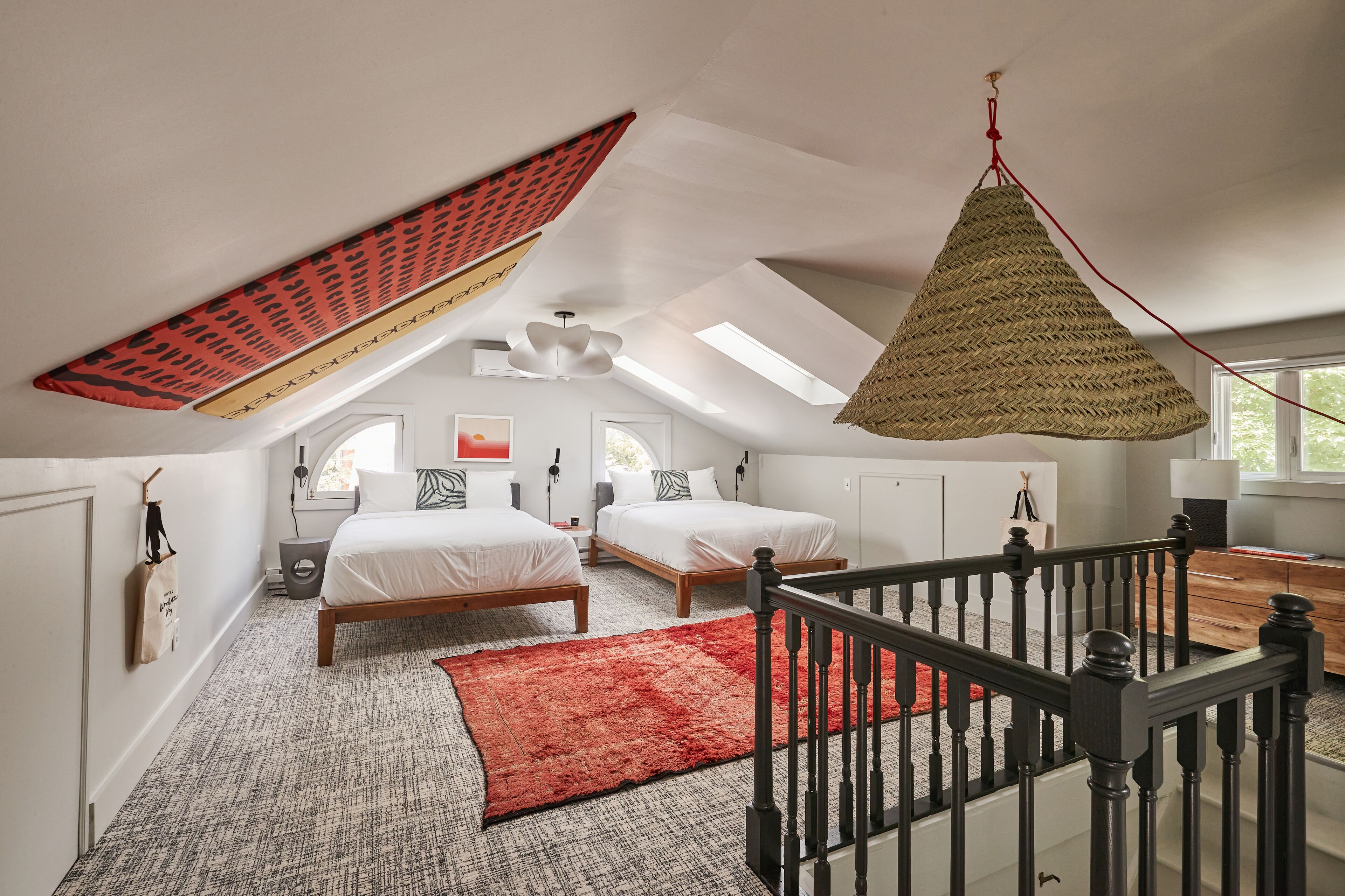 Un dormitorio con dos camas, un tapete rojo, techo de madera y una lámpara colgante.