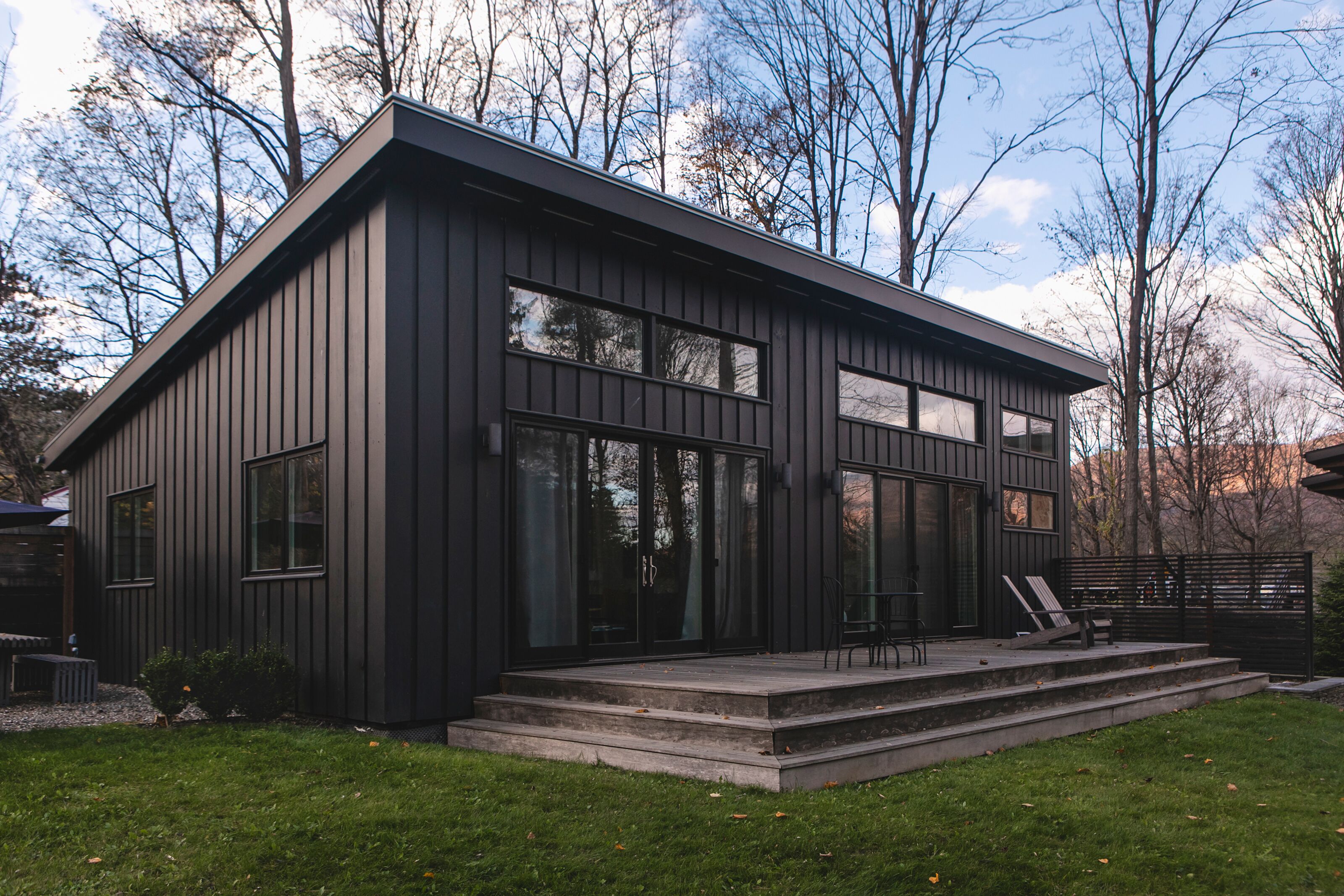 Un bâtiment moderne aux couleurs sombres, doté de grandes fenêtres et d’un espace extérieur couvert aménagé avec des sièges.