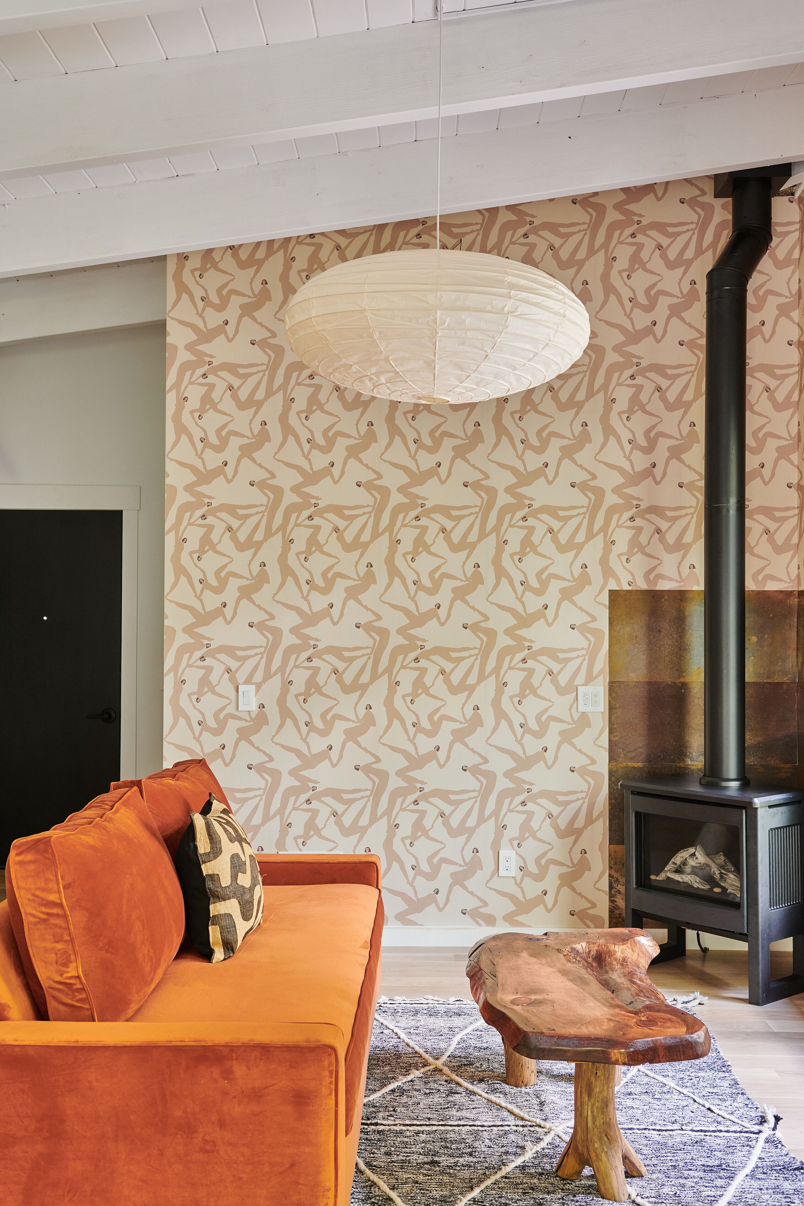A living room with a sofa, a wooden coffee table, a patterned wall, a hanging light fixture, and a fireplace.