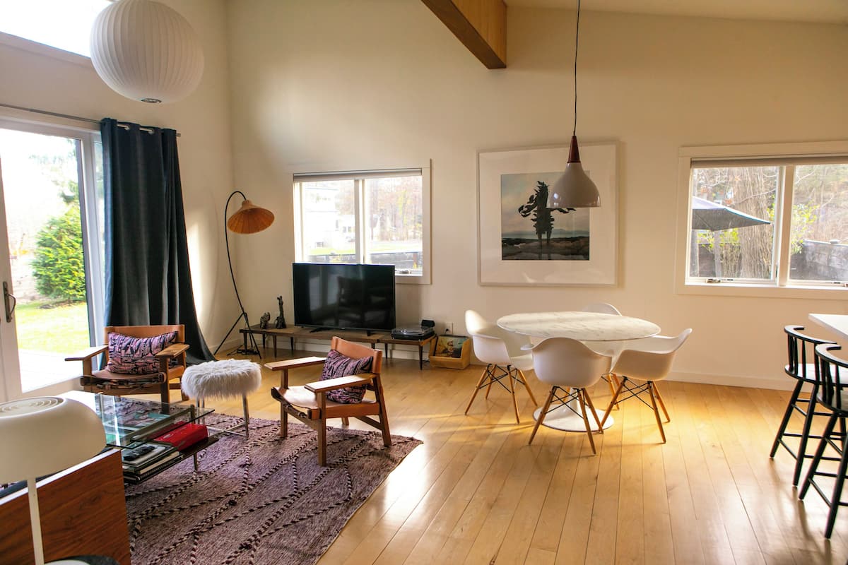 A modern living room with a television, dining area, and large windows.