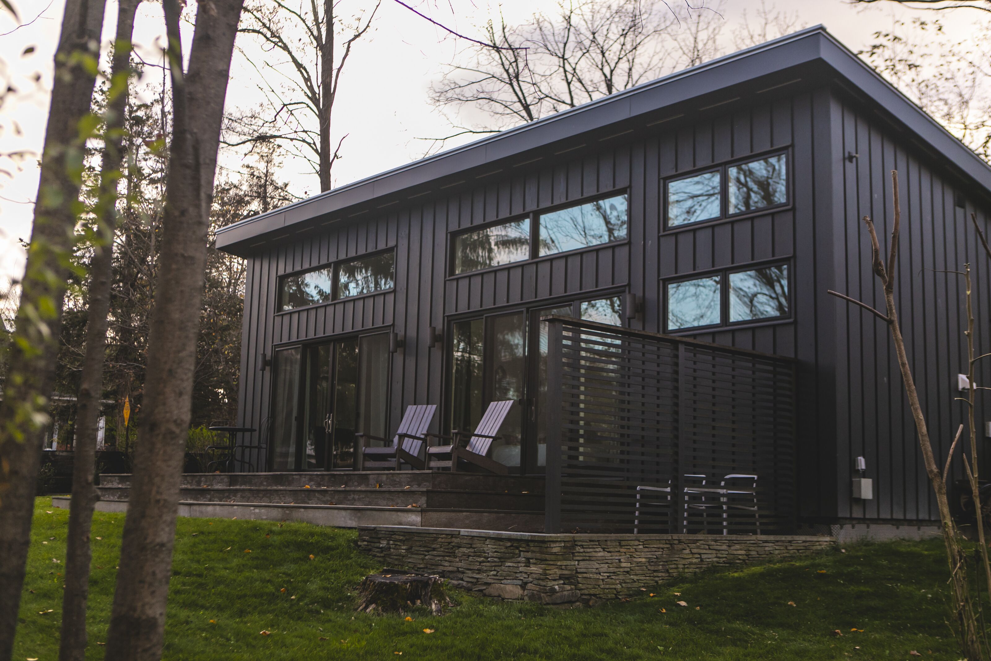 Ein modernes Haus mit Steinfundament, großen Fenstern und einer Veranda mit Sitzgelegenheiten.
