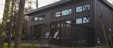 Ein modernes Haus mit Steinfundament, großen Fenstern und einer Veranda mit Sitzgelegenheiten.