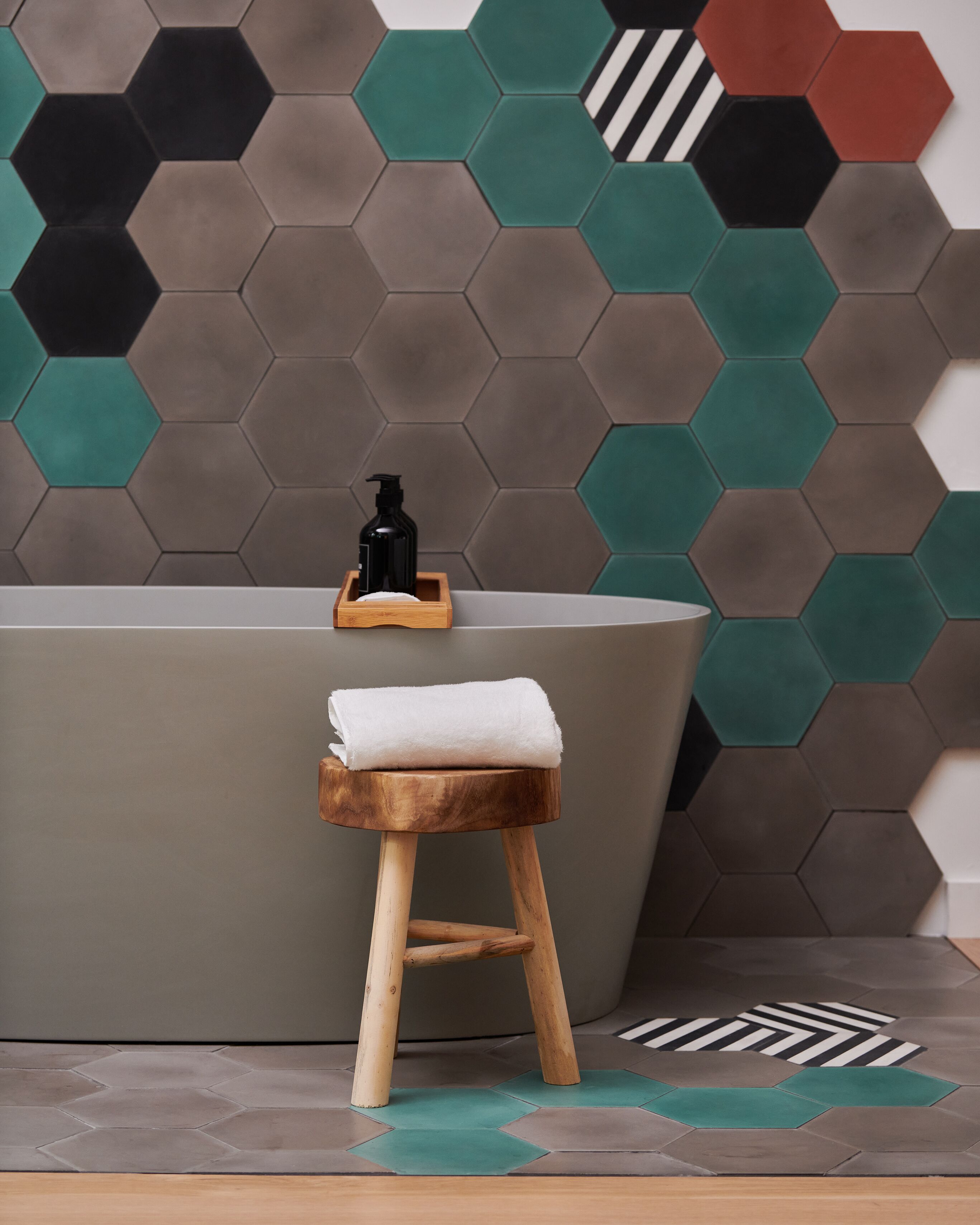 A bathroom with a wooden stool, a white towel, and a black bottle on a wooden tray.