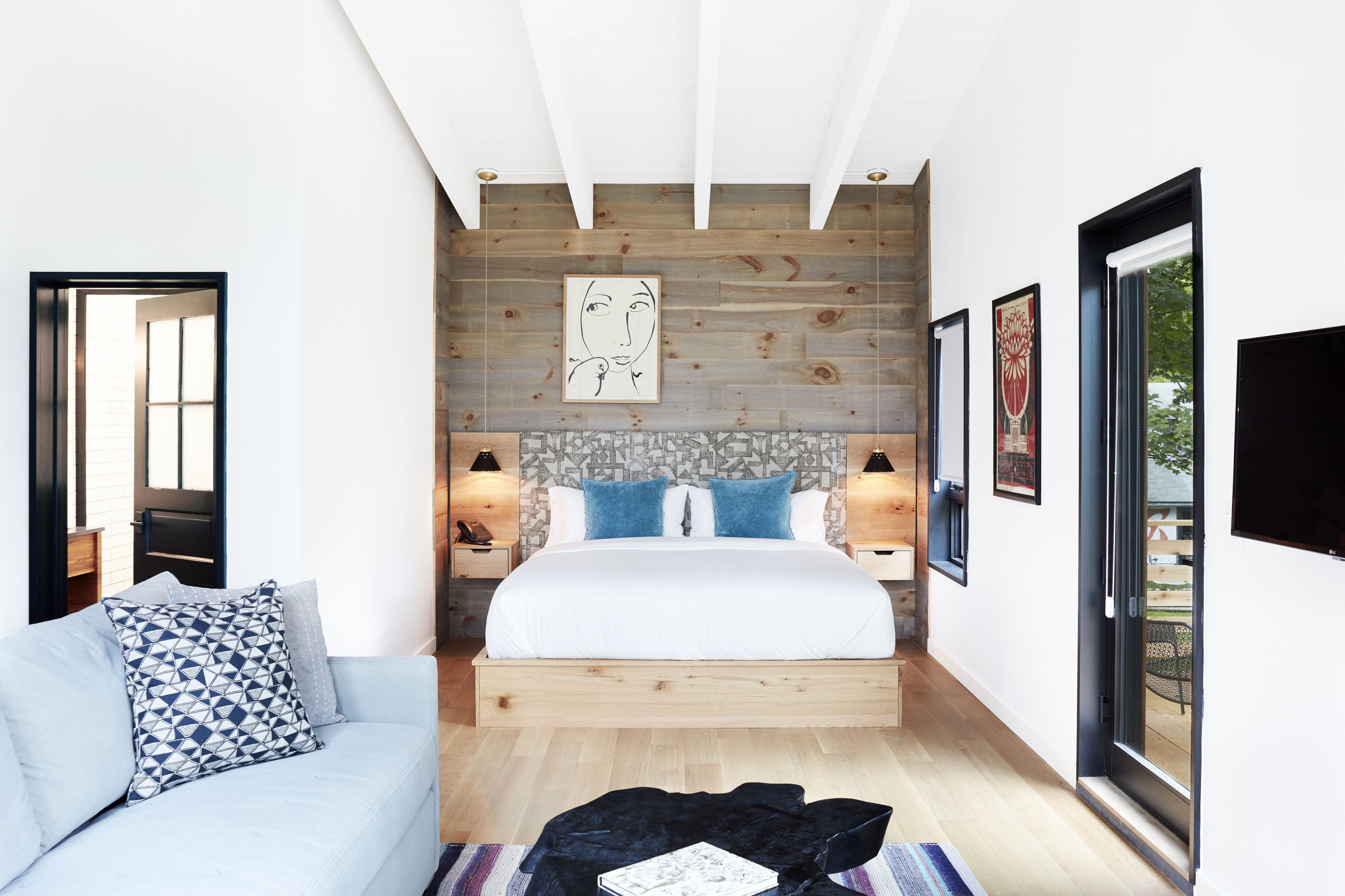 A modern bedroom with a wooden headboard, a large bed, a blue sofa, and a small table with a book.