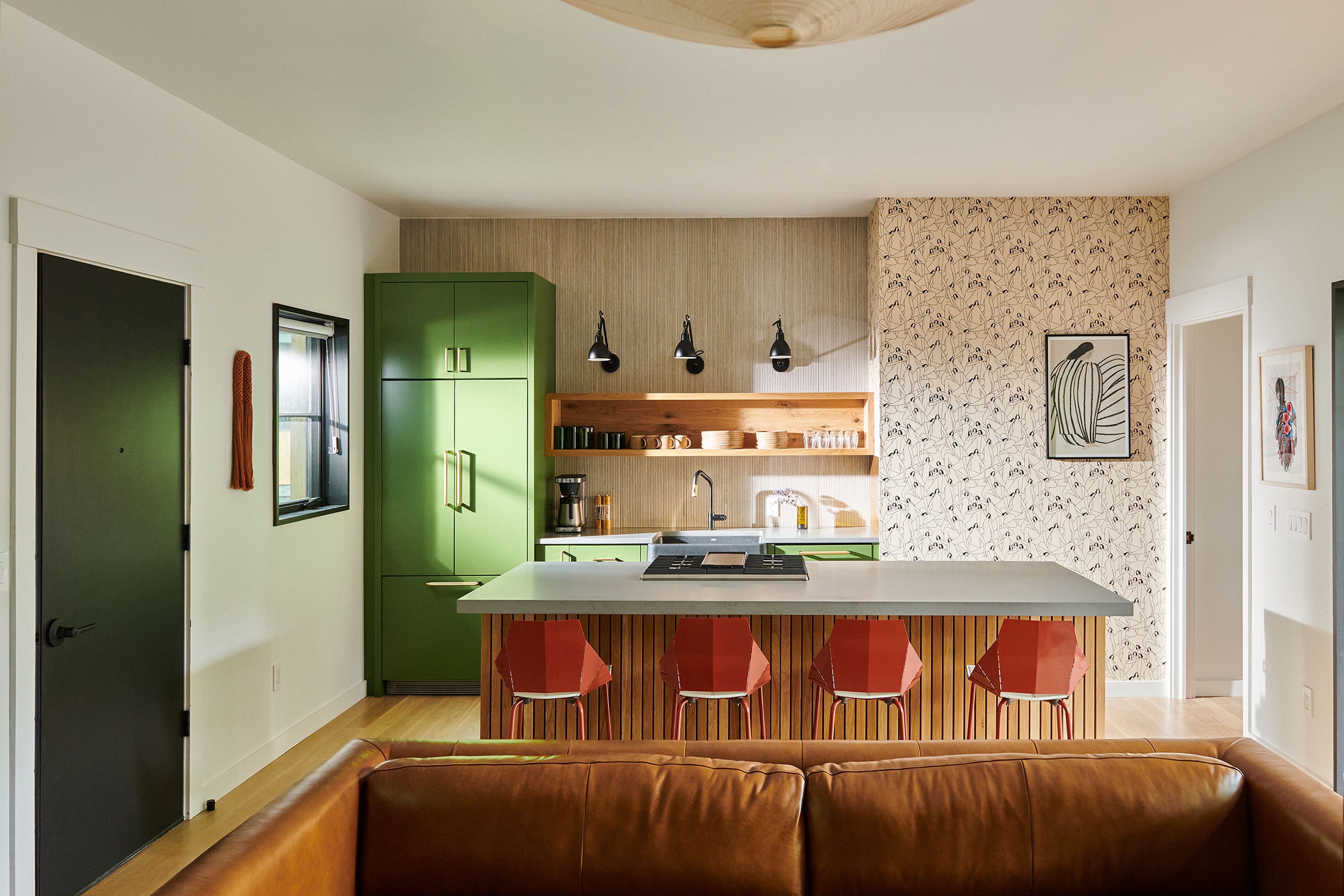 A modern kitchen with a central island, green cabinets, and red bar stools.