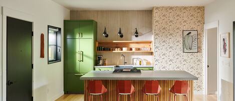 A modern kitchen with a central island, green cabinets, and red bar stools.