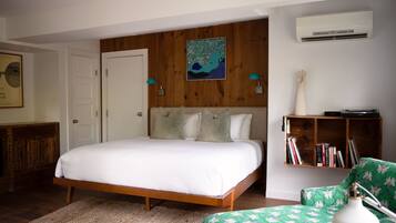 A bedroom with a wooden bed frame, a green patterned chair, a bookshelf, and an air conditioning unit.