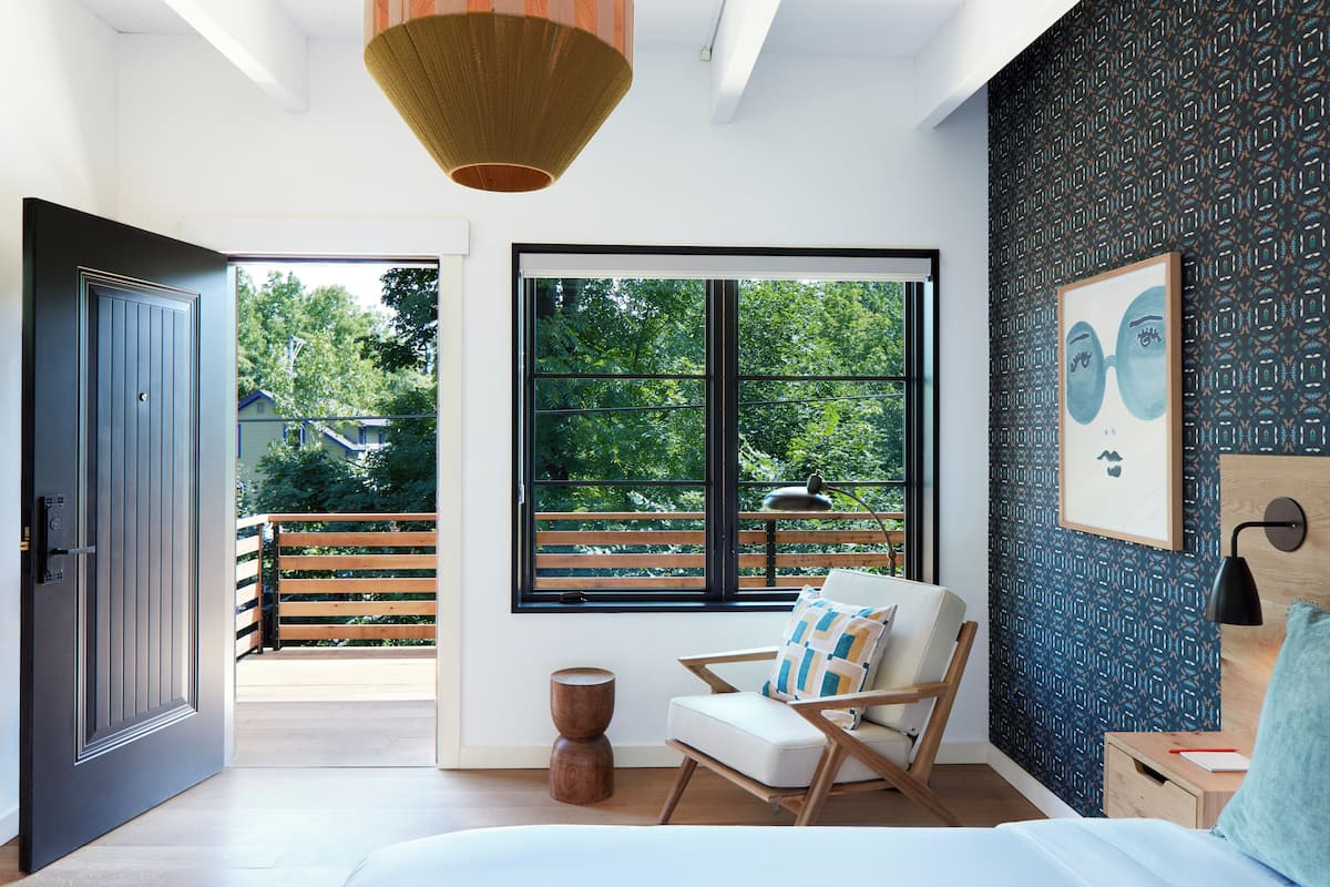 A modern bedroom with a large window, a wooden floor, a bed, a chair, and a small table.
