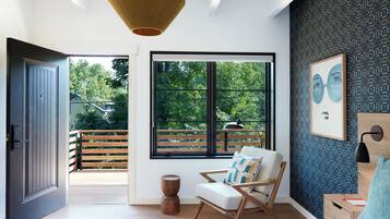 A modern bedroom with a large window, a wooden floor, a bed, a chair, and a small table.