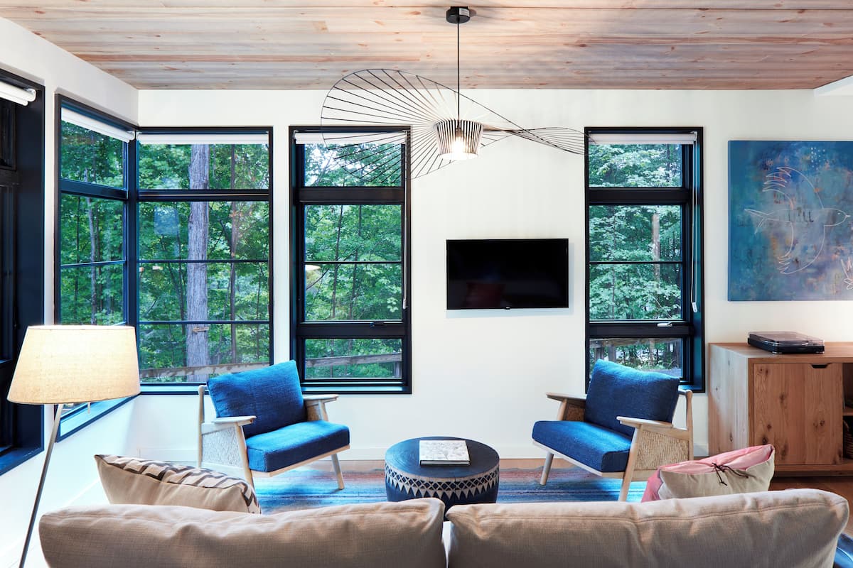 A modern living room with large windows, a flat-screen TV, and a unique ceiling light fixture.