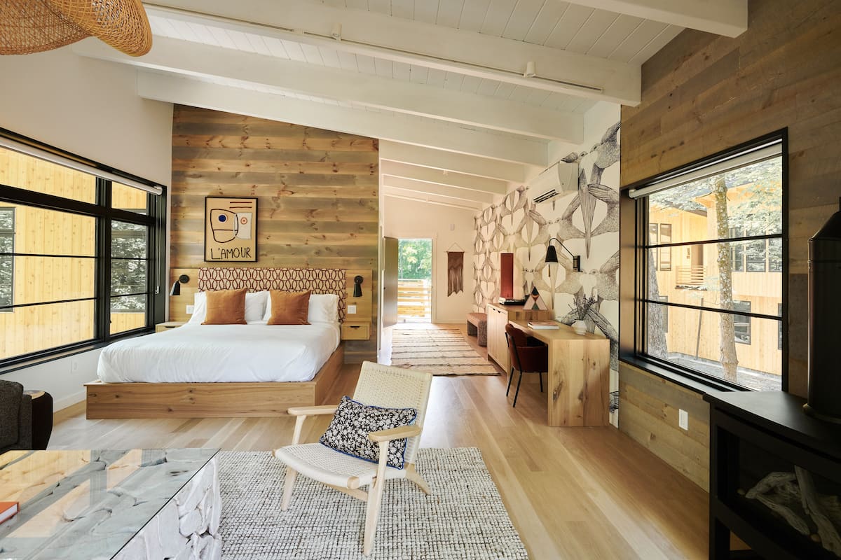 A modern bedroom with a wooden bed, a desk, and large windows.